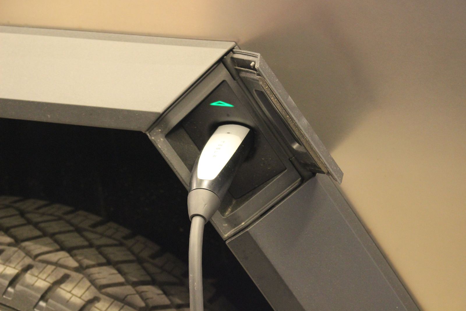 Charging cable plugged into a Cybertruck charge port above the rear wheel